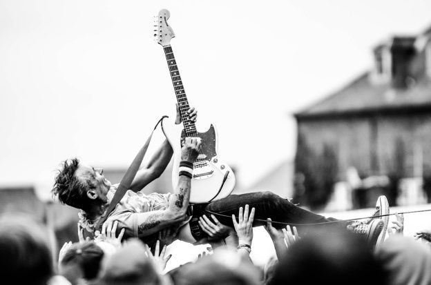 gray scale photo of man lifted by people holding stratocaster guitar
